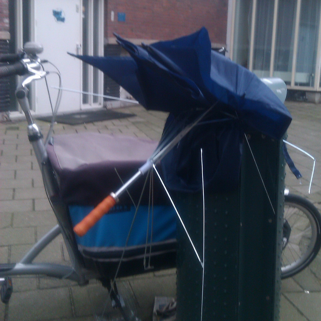 Blue brolly stuffed in city bin. Bin in front of a cargo bike.