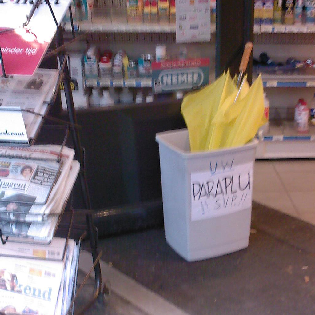 A yellow brolly in a bin (used as a umbrella stand) in front of a shop